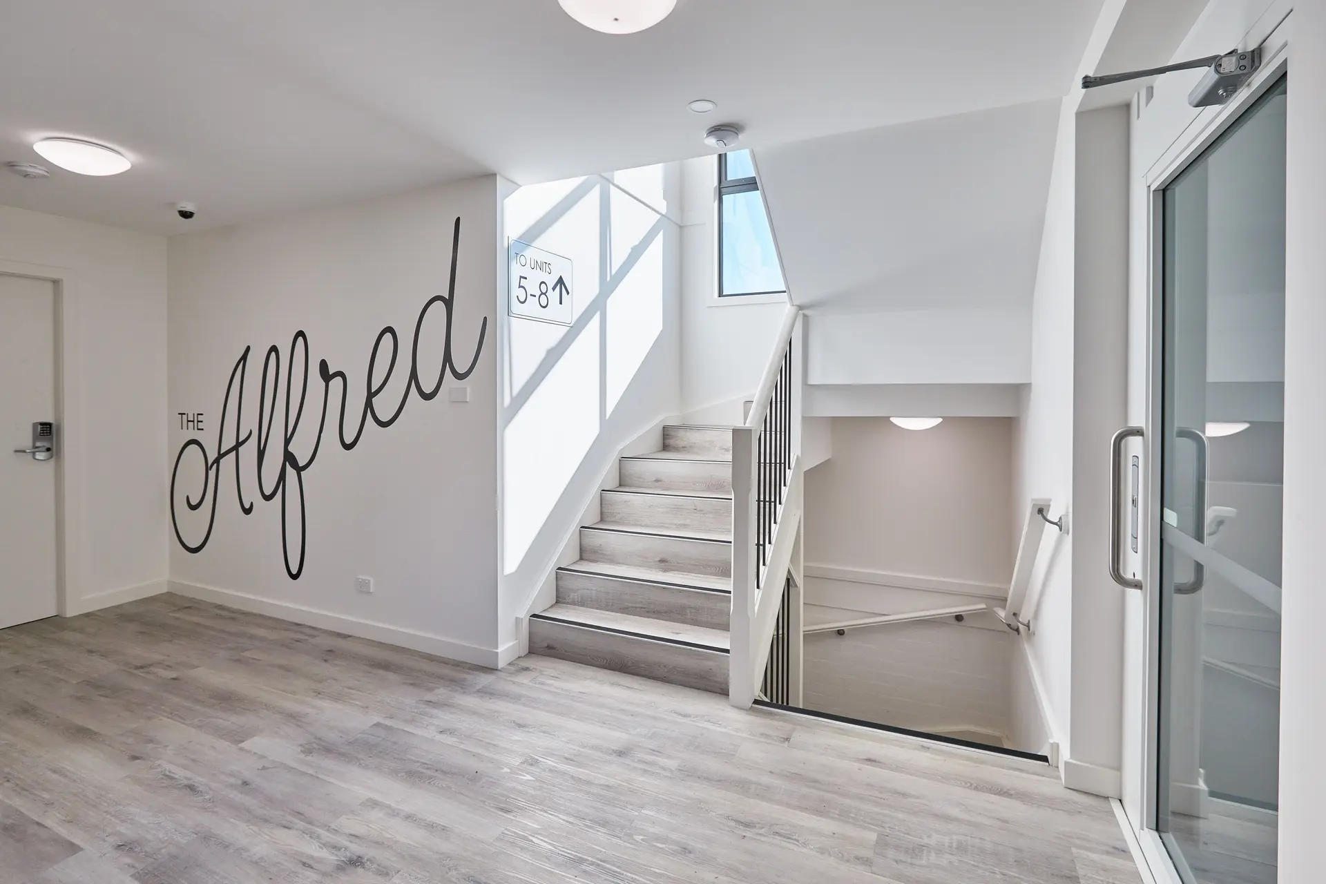 The Alfred Lodge branded entry foyer with light oak floors, glass entry, and unit wayfinding signage